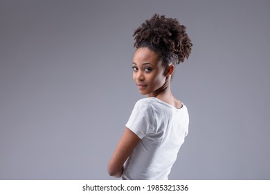 Attractive Slim Young Black Woman Looking Back Over Her Shoulder With An Expectant Serious Expression On A Grey Studio Background With Copyspace