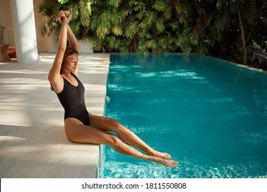 Attractive slim young female stretching, sunbathing alone, being on vacation, having rest at spa resort, enjoying free time, sitting near swimming pool - Powered by Shutterstock