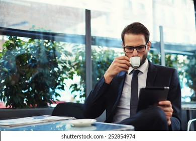 Attractive and smart business man using his tablet while having breakfast at coffee shop, businessman holding cup of coffee while read news on tablet  - Powered by Shutterstock