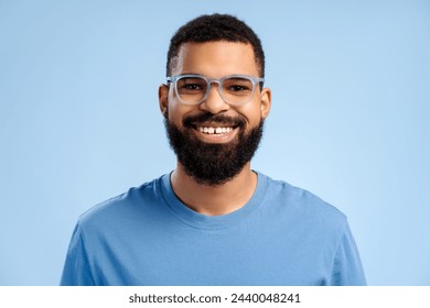 Attractive, smiling, bearded African American man wearing stylish eyeglasses looking at camera standing isolated on blue background. Vision concept, treatment - Powered by Shutterstock