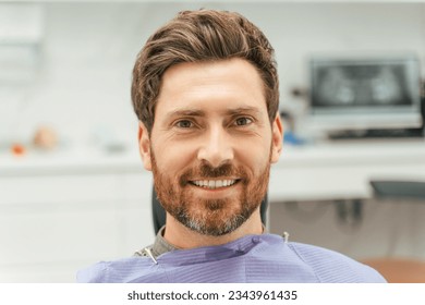 Attractive smiling bearded man sitting in dental chair, looking at camera. Male patient visiting dental clinic - Powered by Shutterstock