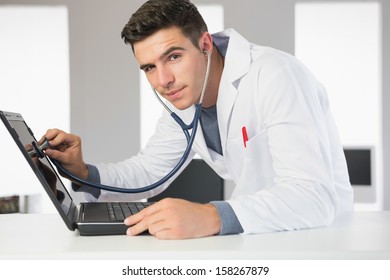 Attractive smiling computer engineer examining laptop with stethoscope in bright office