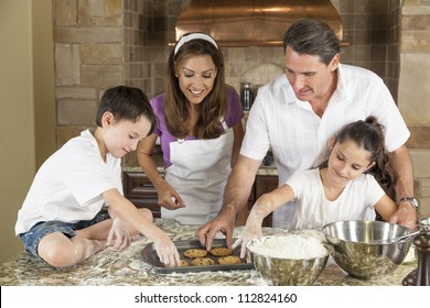 An Attractive Smiling Family Of Mother, Father, And Two Children Baking And Eating Fresh Chocolate Chip Cookies In A Kitchen At Home