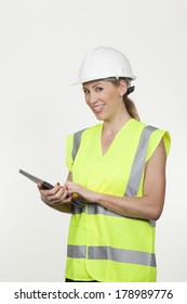 Attractive smiling female architect, structural engineer or safety officer wearing a hardhat and high visibility fluorescent jacket holding a tablet computer in her hands isolated on white