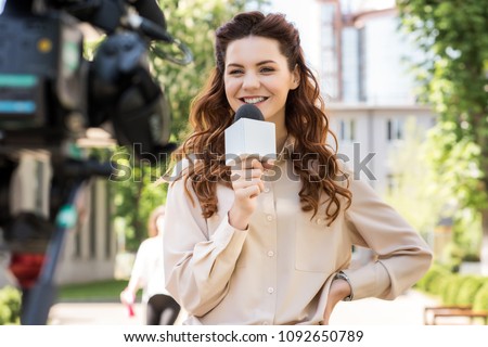 attractive smiling female journalist with microphone talking to digital video camera