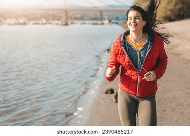 Attractive smiling female with long dark hair wearing tights and jacked while running by the seaside on a sunny cold day in autumn. - Powered by Shutterstock