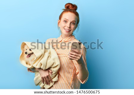 attractive smiling girl with a pet in her hands making a phone call to her friend. close up portrait, isolated blue background, studio shot. lifestyle.interest. hobby
