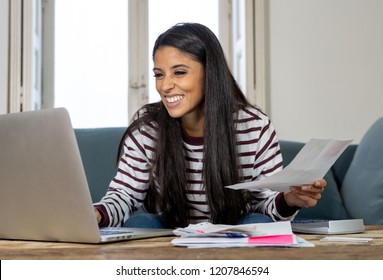 Attractive smiling latin woman paying bills accounting costs charges taxes and mortgage at home using calculator and laptop looking pleased and happy in e-banking and home finance concept.