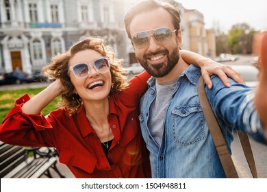 attractive smiling man and woman traveling together, stylish couple in love taking selfie photos on phone on romantic trip, sunny autumn city, wearing shirt, sunglasses, travelers having fun