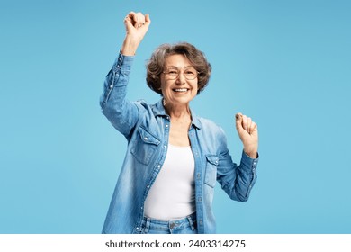 Attractive smiling senior, happy modern grandmother woman holding hands up dancing celebration success isolated on blue background. Good news, positive lifestyle concept - Powered by Shutterstock