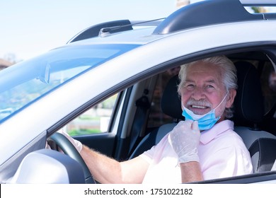 Attractive Smiling Senior Man With Protective Gloves Driving Silver Car Moves Away From Face Mask Against Coronavirus - New Normal Life Until End Of Pandemic