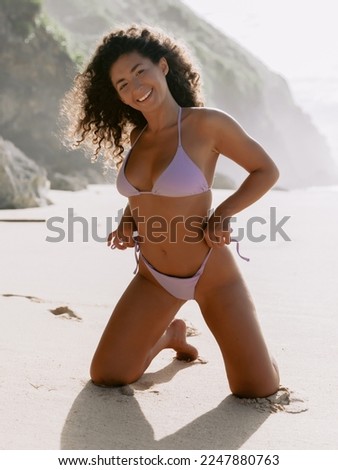 Attractive smiling woman in bikini with tanned body posing on beach, beautiful model in bikini