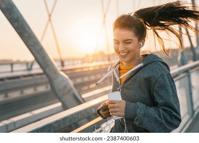 Attractive smiling woman promoting healthy lifestyle by jogging outdoors. Happy woman doing morning fitness routine while listening to music. - Powered by Shutterstock