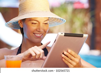 Attractive smiling woman with straw hat using tablet computer in pool - Powered by Shutterstock