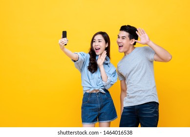 Attractive Smiling Young Asian Couple Having Video Call With Their Family On Smartphone Isolated On Yellow Studio Background