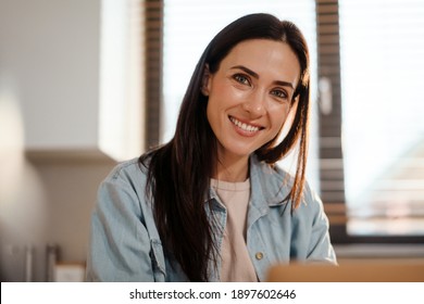 Attractive smiling young smart woman working on laptop computer while spending time at home in the kitchen, close up