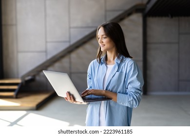 Attractive Smiling Young Woman Using Laptop Computer While Standing In A Stylish Living Room