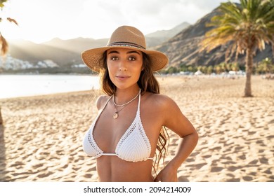 Attractive spanish brunette woman in the knitted white bikini and hat relaxing on the tropical beach. Portrait. Natural girl enjoying sunny day. 