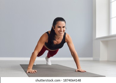 Attractive Sports Woman Holding A Plank And Doing Press Exercises In A Bright Gym. Female Fitness Instructor Conducts Training. Yoga And Healthy Lifestyle.