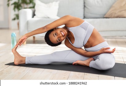 Attractive Sporty Black Woman Doing Warming Up Stretching Exercses On Yoga Mat In Her Home Gym. Positive Millennial Lady Bending To Her Leg, Working Out Muscles Flexibility