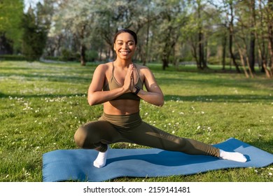 Attractive sporty black woman doing warming up stretching exercses on yoga mat at urban park, copy space. Positive African American lady working out muscles flexibility outdoors