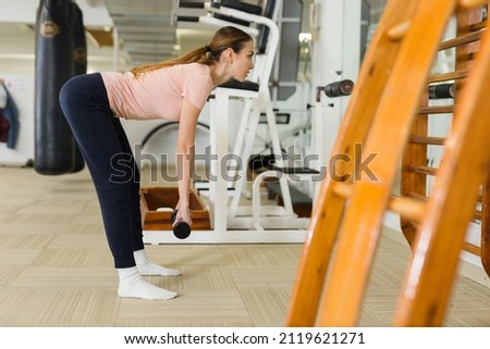 Attractive sporty girl doing leg and glute workout in gym, performing romanian deadlift with dumbbells. Concept of weight training for women