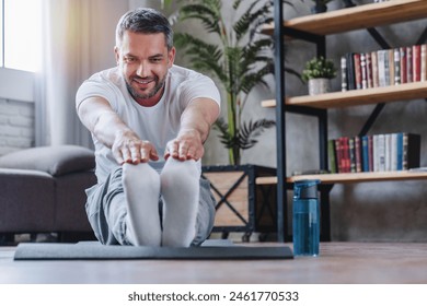 Attractive sporty man stretching his legs at flat. Home training. Concept of sport, health, action, nutrition. Copy space for ad. Portrait of middle age sportive human guy doing stretching. - Powered by Shutterstock