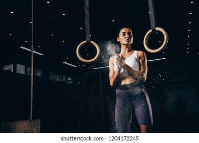 Attractive Sporty Woman Clapping Hands With Talc Before Workout With Gymnastic Rings