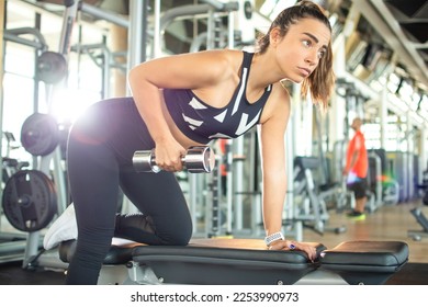 Attractive sporty woman flexing muscles with dumbbell in gym. - Powered by Shutterstock