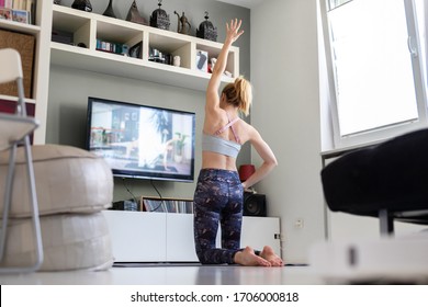 Attractive Sporty Woman Working Out At Home, Doing Pilates Exercise In Front Of Television In Her Living Room. Social Distancing. Stay Healthy And Stay At Home During Corona Virus Pandemic.