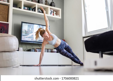 Attractive Sporty Woman Working Out At Home, Doing Pilates Exercise In Front Of Television In Her Living Room. Social Distancing. Stay Healthy And Stay At Home During Corona Virus Pandemic.