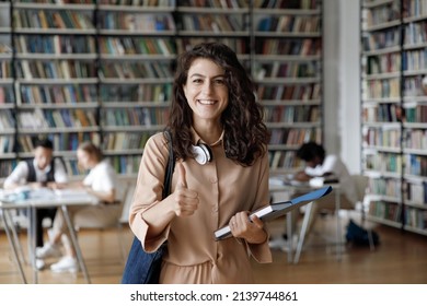 Attractive student 18s girl standing in library showing thumbs up, enjoy interesting effective studies in higher institution. Successful excellent learner, scholarship, good quality education concept - Shutterstock ID 2139744861
