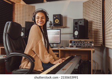 Attractive stylish African American female musician sound engineer playing synthesizer while working in recording studio - Powered by Shutterstock