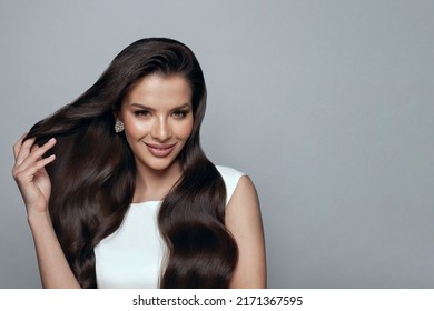 Attractive stylish happy brunette woman with long wavy hair touсhing her hair on white. Hair care and beauty concept. 