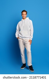 Attractive stylish man wearing white sweatshirt and sweatpants standing over blue studio background
