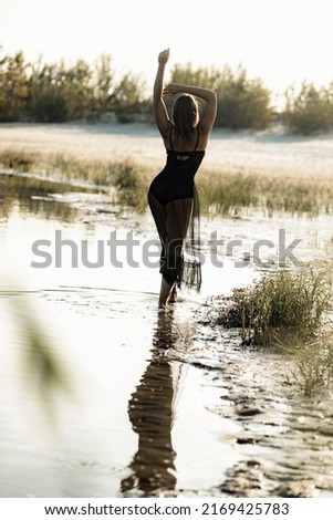 Attractive stylish middle aged woman posing on beach of lake at sunset