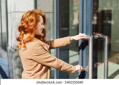 Attractive Stylish Redhead Woman Unlocking The Double Doors To A Commercial Building As She Opens Up For Work In The Morning