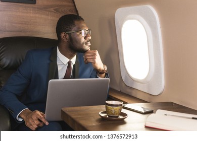 Attractive and successful African American businessman with glasses working on a laptop while sitting in the chair of his private jet.