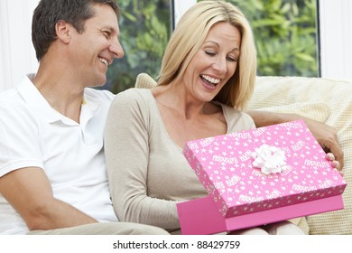 Attractive, Successful And Happy Middle Aged Man And Woman Couple In Their Forties, Celebrating Her Birthday Opening A Present In A Pink Gift Box.