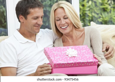 Attractive, Successful And Happy Middle Aged Man And Woman Couple In Their Forties, Celebrating Her Birthday Opening A Present In A Pink Gift Box.