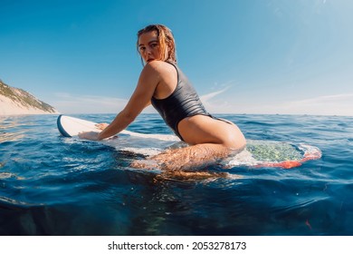 Attractive surf girl on surfboard in blue ocean. Blonde sexy surfer woman look at camera