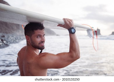 Attractive surfer smiles with his surfboard resting on his head, he is at the beach. Sporty and muscular caucasian man - Powered by Shutterstock