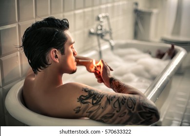Attractive tattooed guy smoking a cigarette in the tub
