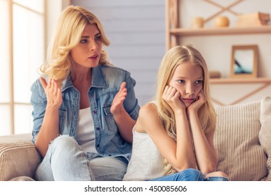 Attractive teenage girl is looking sadly away, leaning on her hands while her mother is scolding her, sitting on couch at home