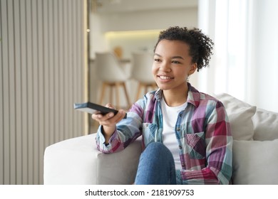 Attractive Teenage Girl Is Watching It And Shifts Channels With Remote Controller. Reality Show Or Series Watching. Positive African American Or Hispanic Young Woman Has Weekend Leisure At Home.