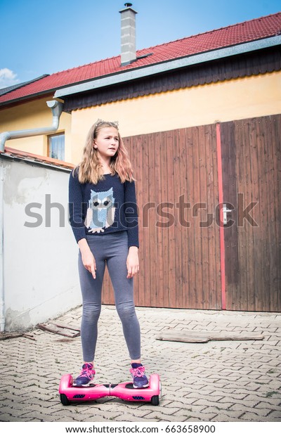 Attractive teenage girl in wise owl fashion sweater\
standing on her pink mini electric self-balancing board scooter on\
battery power for eco city transport next to grunge closed car\
garage door.
