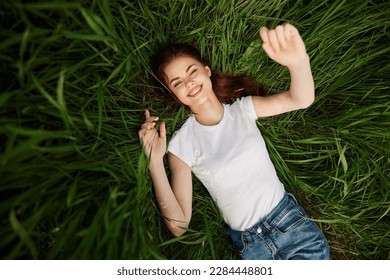 attractive teenager lying down on green grass with hands rised up to the air