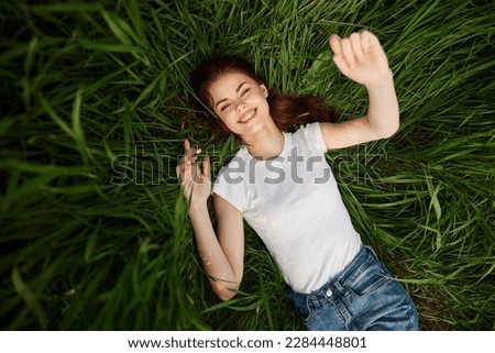 attractive teenager lying down on green grass with hands rised up to the air