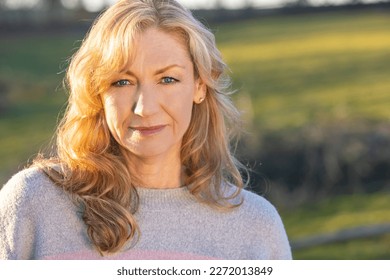 Attractive thoughtful middle aged woman outside smiling in golden hour sunlight - Powered by Shutterstock