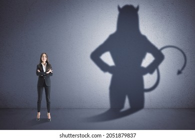 Attractive Thoughtful Young European Woman With Devil Shadow Standing In Empty Concrete Interior. Disguise, Demon And Career Concept